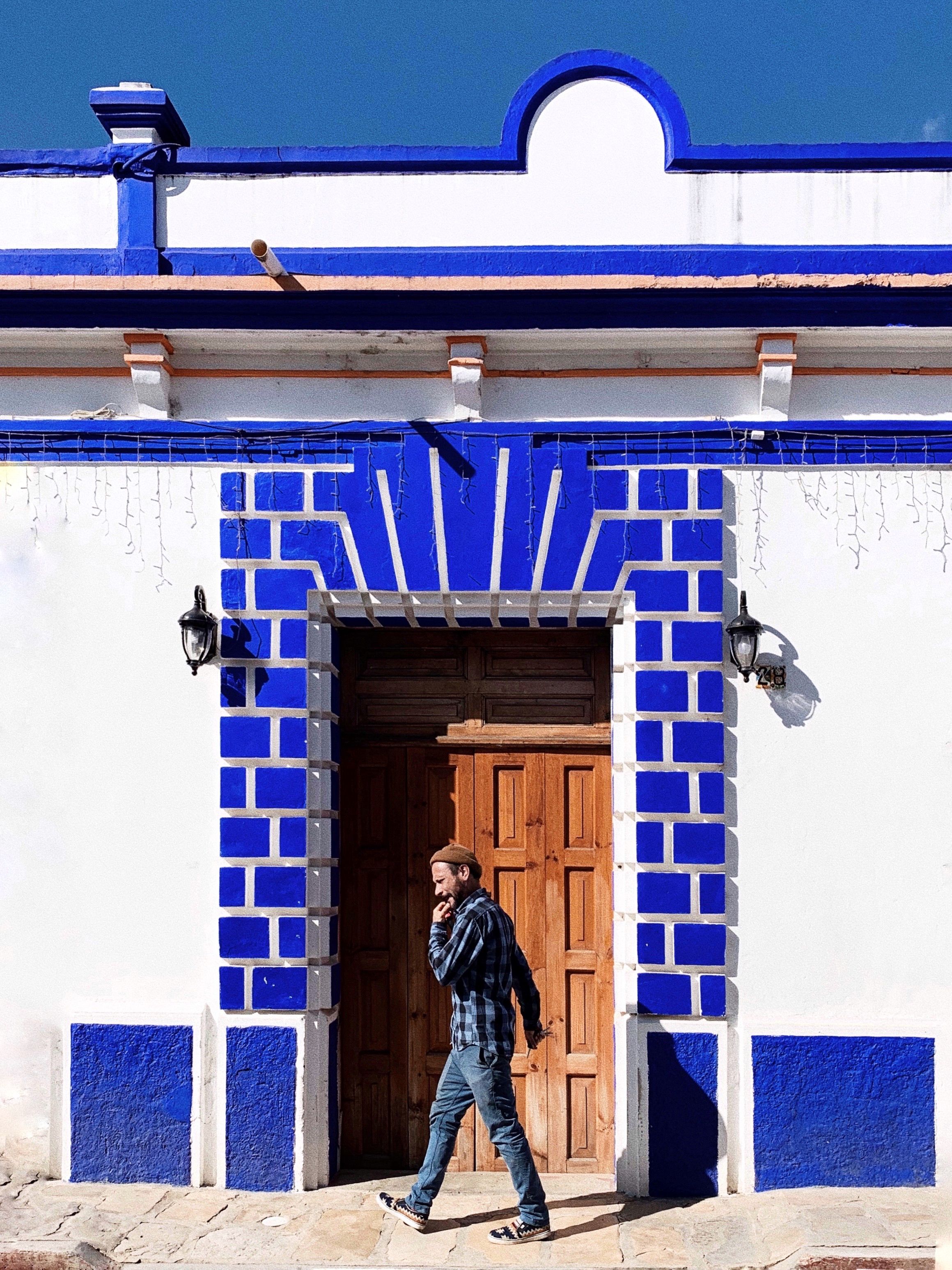 Man walking by a vibrant blue and white entrance in San Cristobal de las Casas, Mexico.