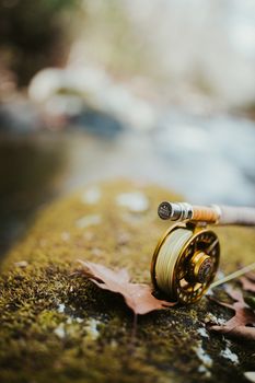 Fly fishing rod and reel resting on a mossy rock by a calm stream, perfect for nature lovers.