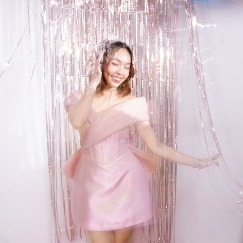 A Woman in Pink Cocktail Dress Standing Beside Glittering Tinsel