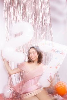 A joyful young woman in a pink dress celebrating her 27th birthday with balloons.