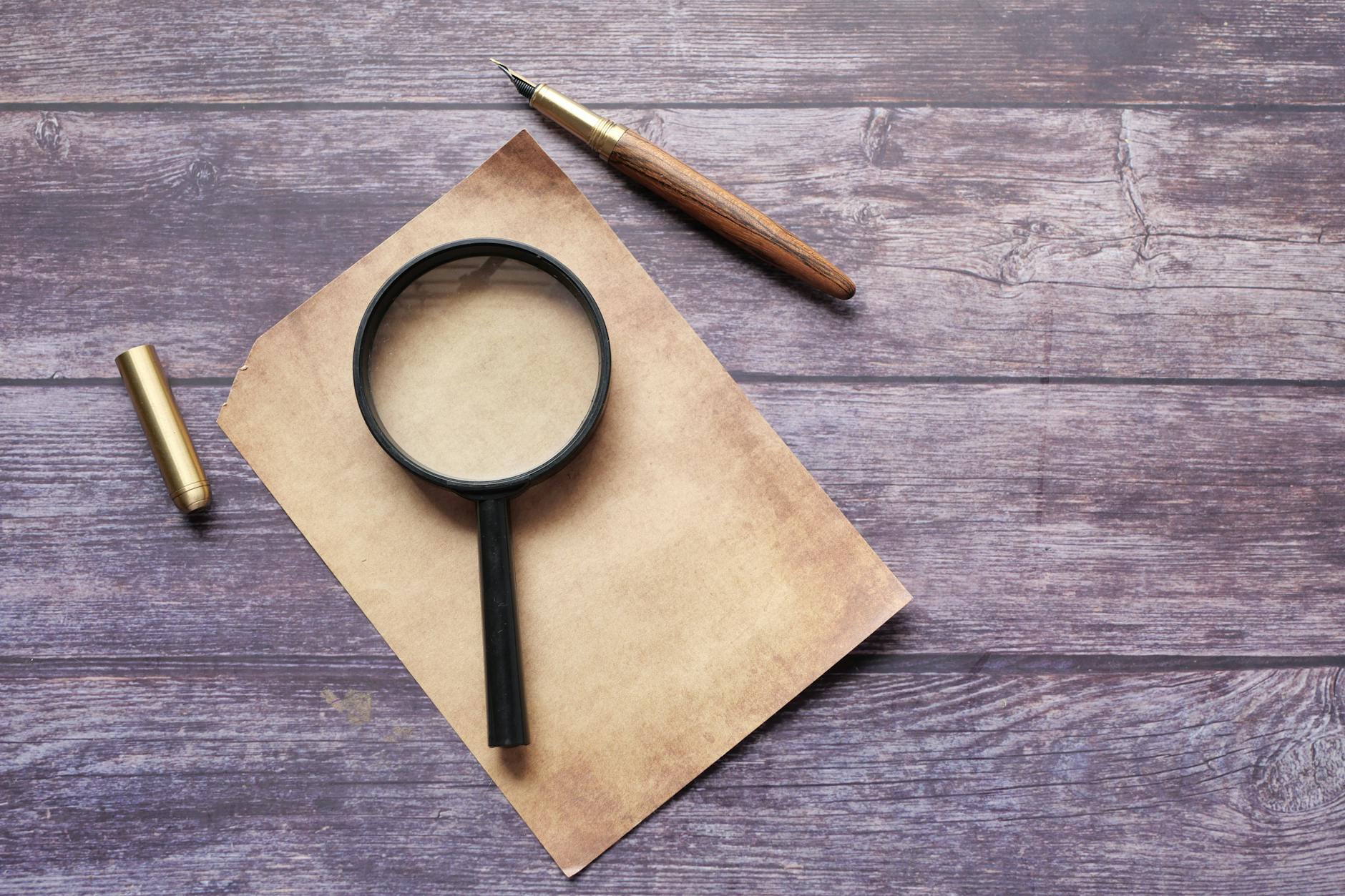 Magnifier and a Quill Pen on an Empty Paper Sheet 