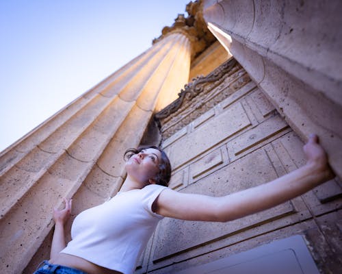 Low Angle Shot of a Woman Standing Between Roman Columns