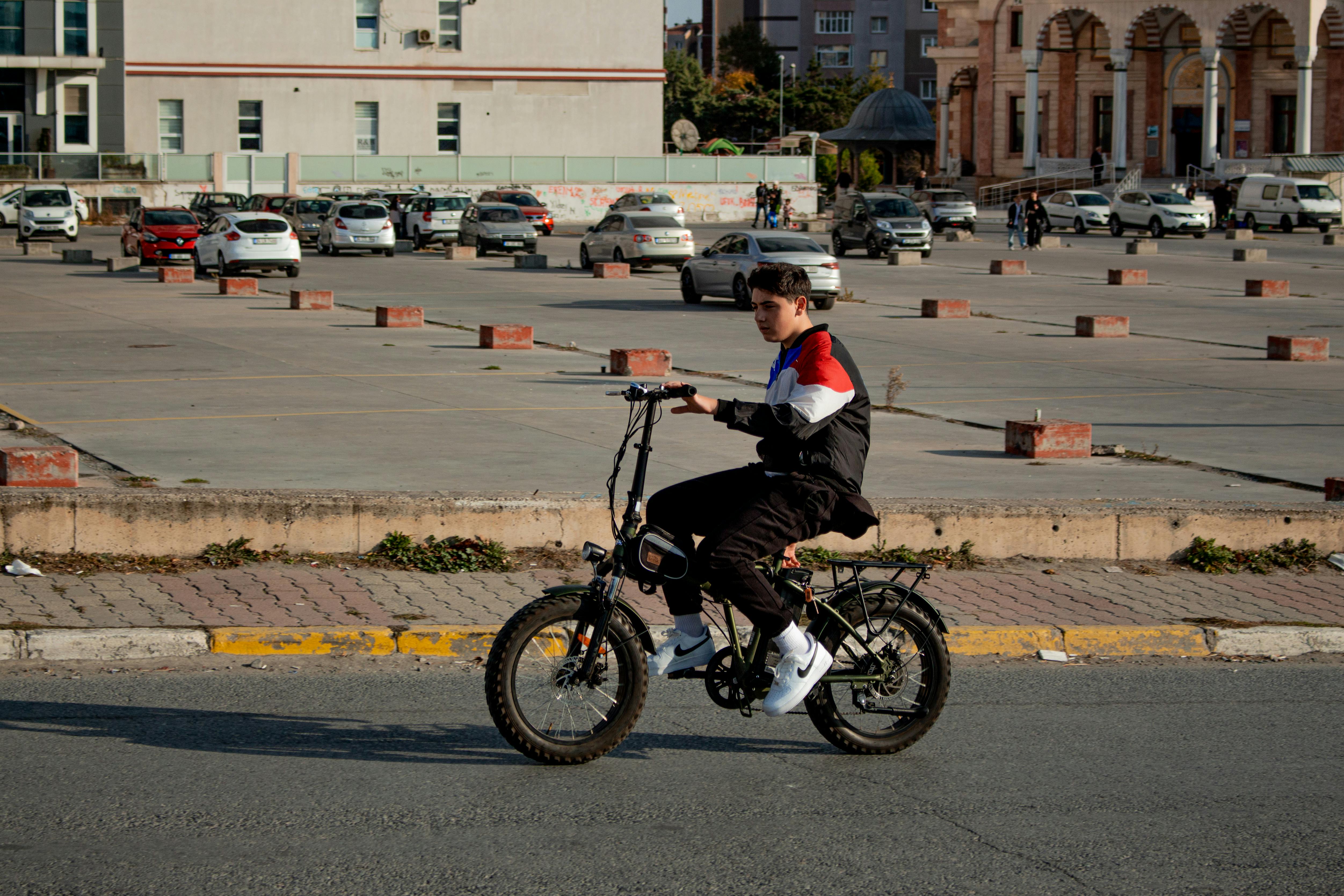 A young boy rides an electric bicycle in a city parking lot under daylight.