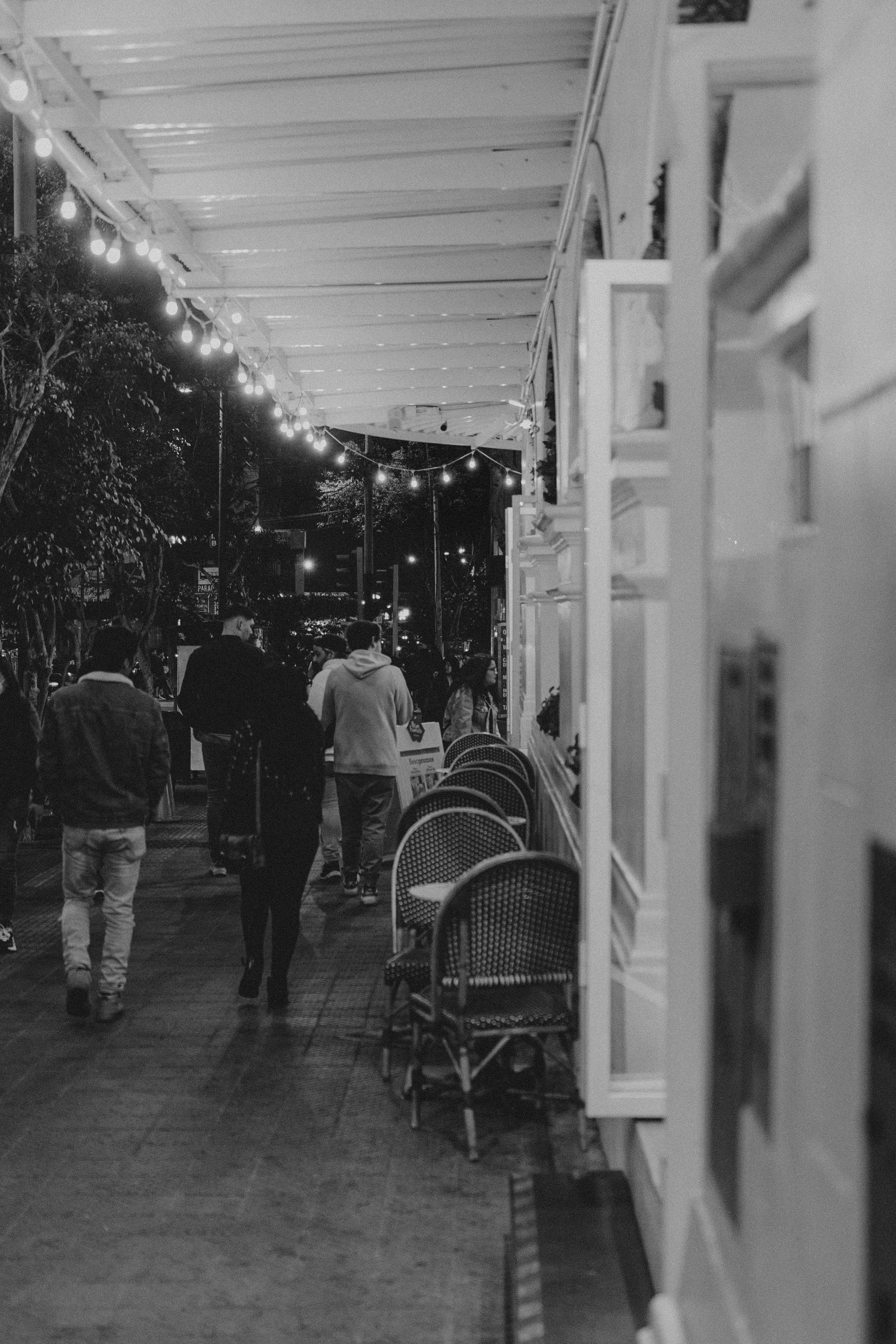Black and white image capturing people walking along a lively Lima sidewalk at night.