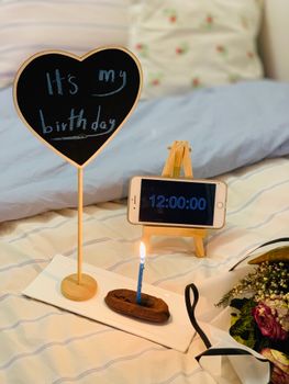 A cozy birthday setup featuring a candle, flowers, and a time display reading noon.