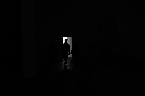 Free A shadowy figure stands silhouetted in a doorway, outlined by bright light. Stock Photo