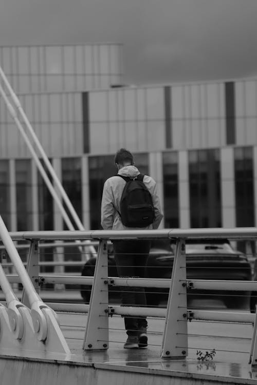 Grayscale Photo of Person Walking near a Railing