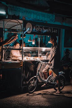 Man on bicycle at illuminated sushi food stall at night, urban ambience.