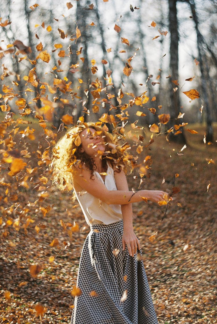 Woman Tossing Autumn Leaves In The Forest And Smiling 