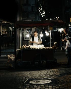 Urban scene featuring a street vendor at night under glowing lights.