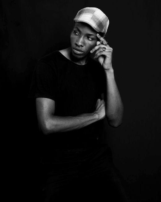 Grayscale portrait of pensive man wearing flat cap against dark background.