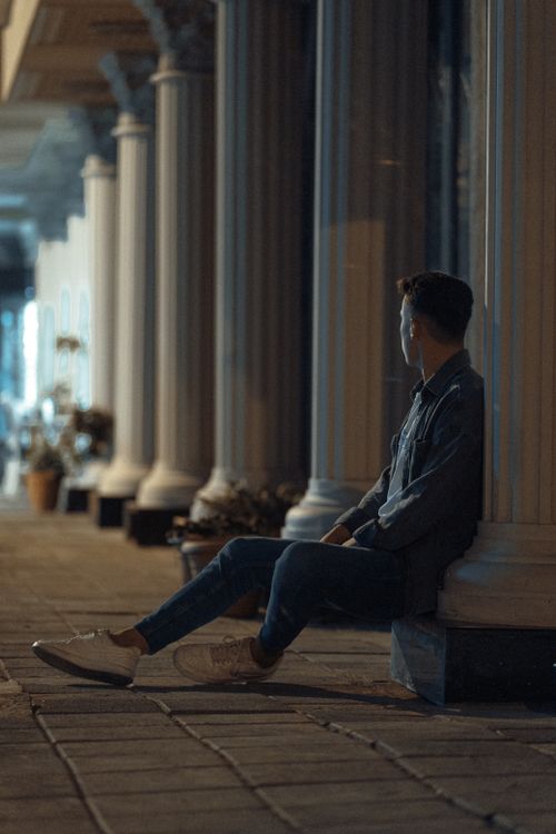 Free A thoughtful man sitting among illuminated columns at night, reflecting solitude. Stock Photo