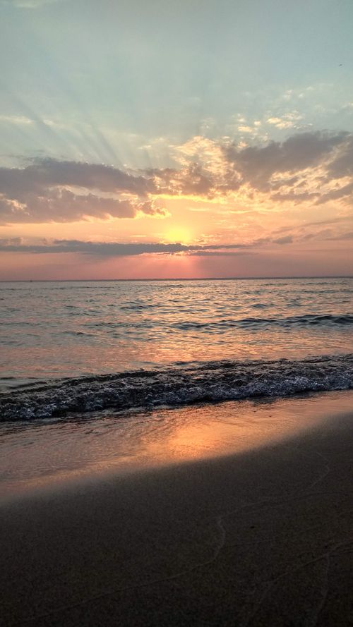 Free A calming sunset view over the ocean waves with a vibrant cloudy sky and warm reflections on the water. Stock Photo