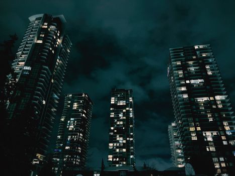 Illuminated skyscrapers towering against a dark, cloudy night sky.