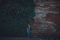 一名年轻女子在爬满常春藤的砖墙边摆出姿势，营造出忧郁的氛围