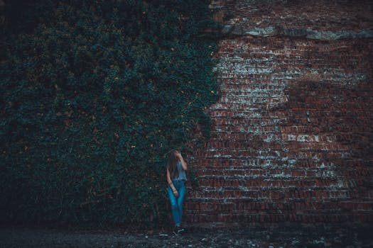 一名年轻女子在爬满常春藤的砖墙边摆出姿势，营造出忧郁的氛围