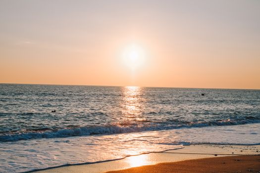 Capture of a serene ocean sunset with golden hues reflecting on tranquil waters and sandy beach.