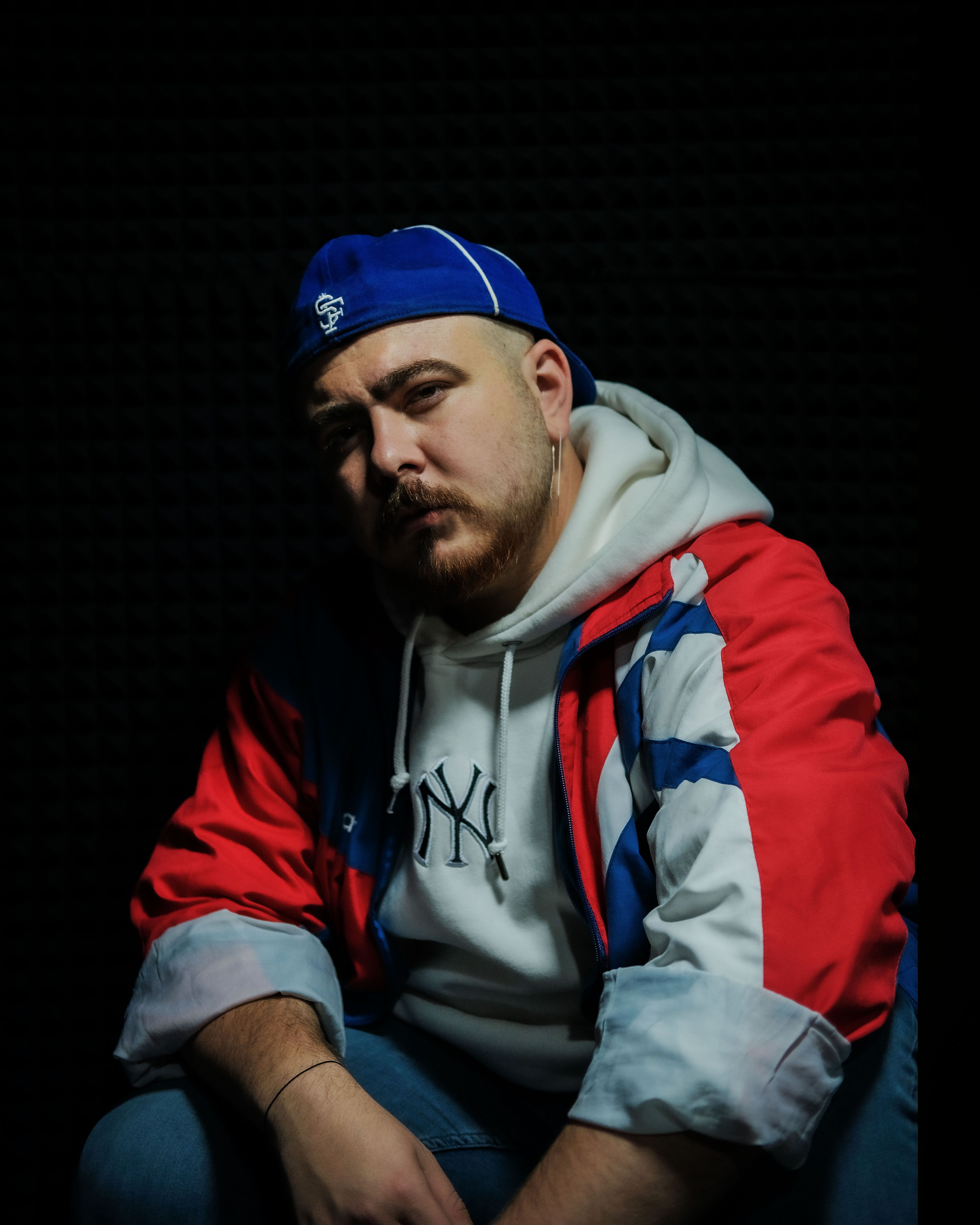 A man in a sporty outfit posing confidently against a dark background, showcasing modern street fashion.