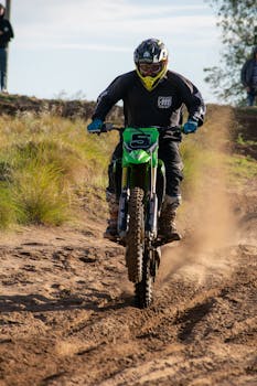 Motocross rider in action on a dirt track, kicking up dust under a clear sky.