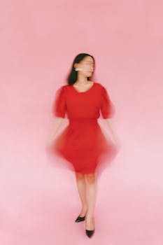 Artistic blurred portrait of woman in red dress against pink studio backdrop.