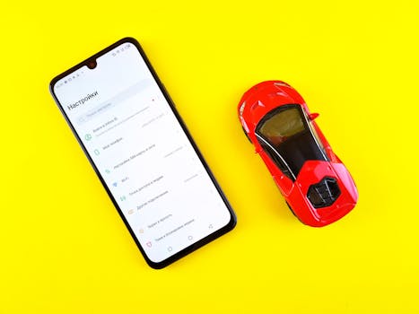 A smartphone and toy car placed on a bright yellow background viewed from above.