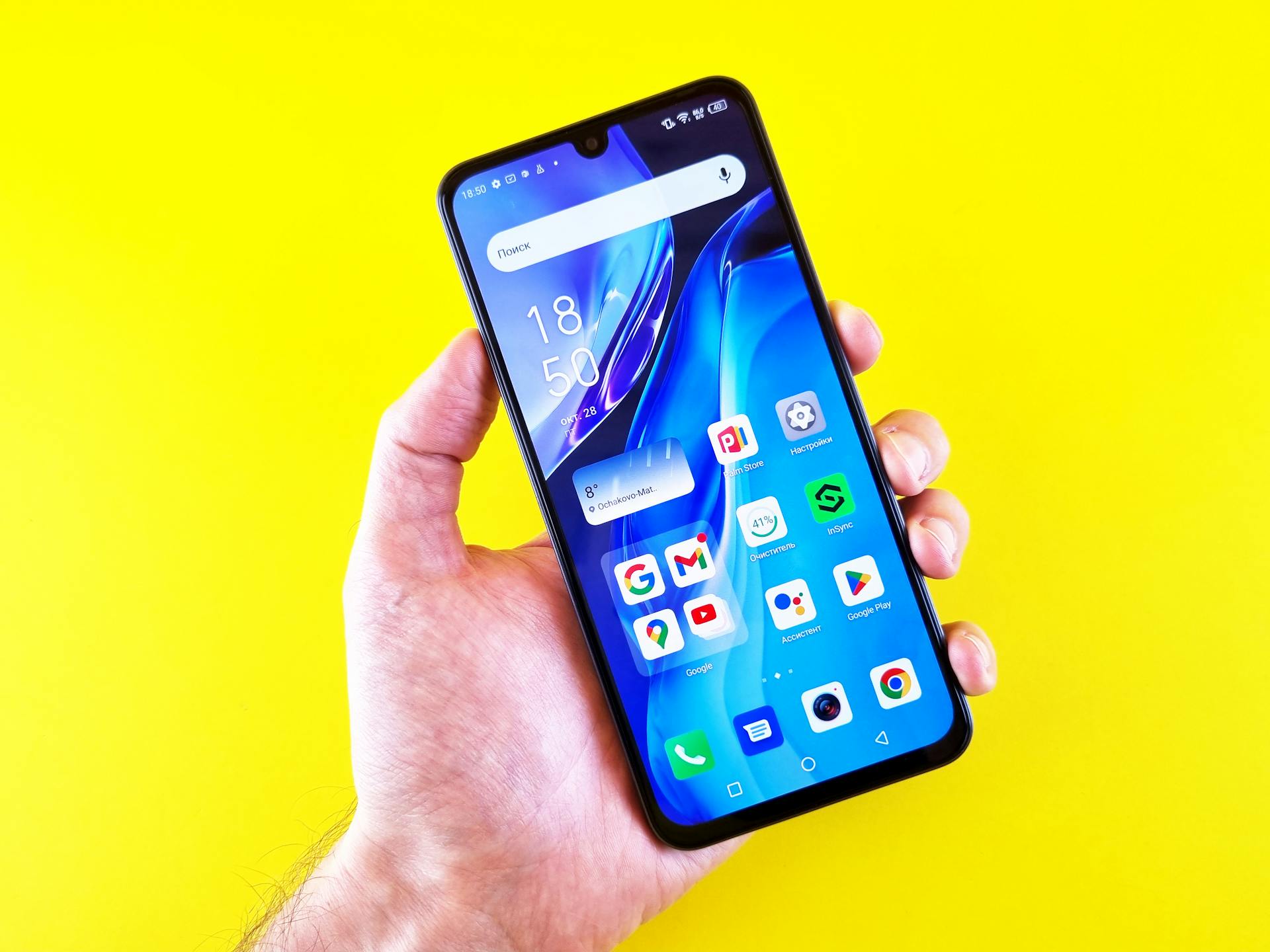 Close-up of a hand holding a smartphone with apps displayed on a bright yellow background.