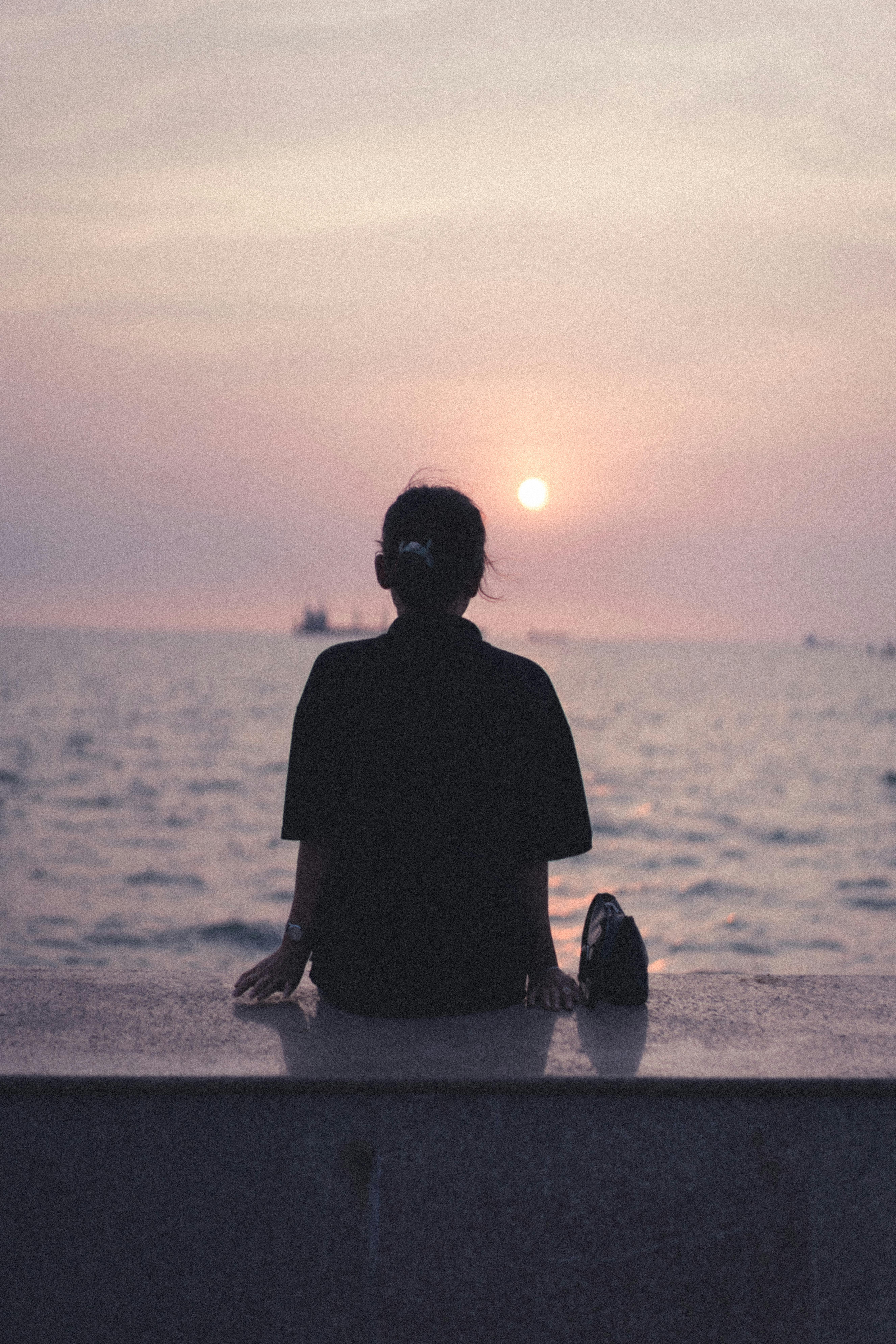 Woman sits by the sea at sunset, enjoying the tranquil ocean view.