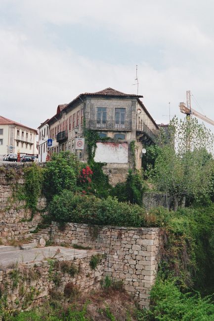 Scenic view of an ancient building covered with ivy along a lush riverbank in Portugal.