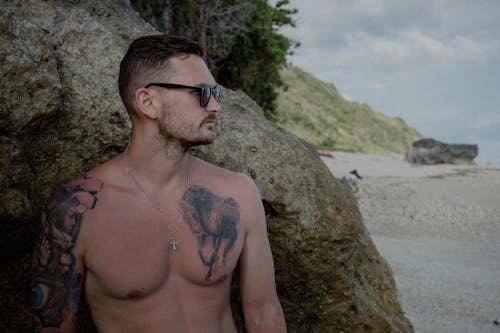 Topless Man Wearing Black Sunglasses Standing Beside Brown Rock