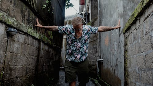 Man in Floral Shirt and Green Shorts Standing in Between Concrete Walls