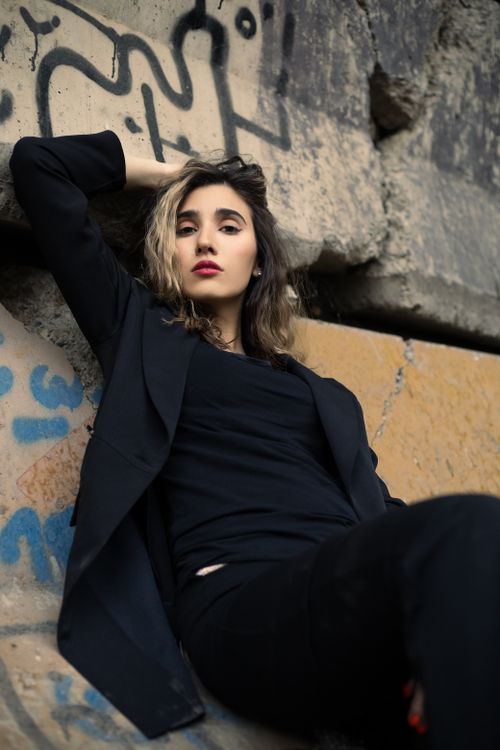 Free Fashionable woman in black blazer and pants posing against a graffiti-covered concrete wall. Urban street style. Stock Photo