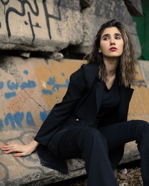 Free A fashionable woman in a black blazer sits against a graffiti wall. Stock Photo