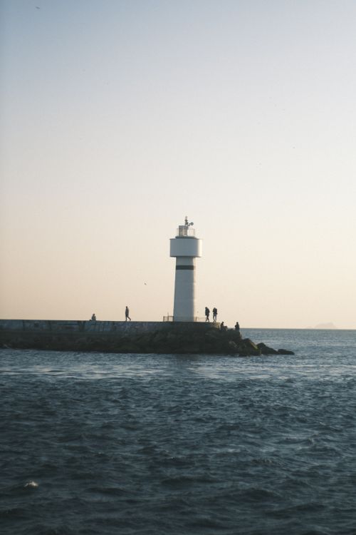 Free A tranquil lighthouse stands by the ocean as dawn breaks over calm waters. Stock Photo