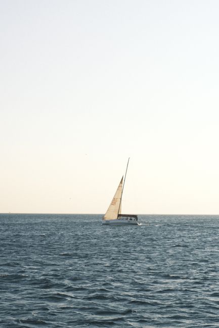 A solitary sailboat glides gracefully across a calm ocean under a clear sky, embodying peace and freedom.