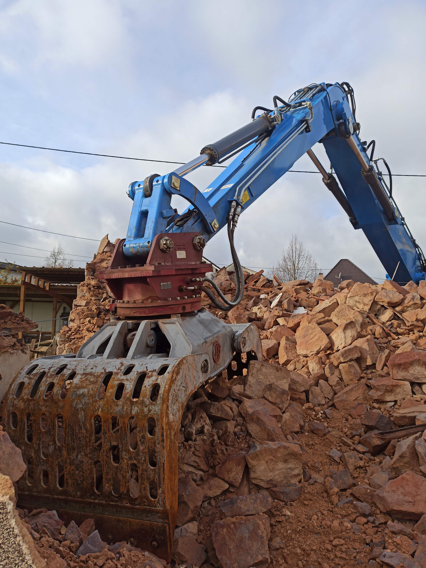 Excavator clearing rubble at a construction site under a cloudy sky