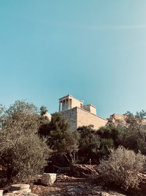 Free View of the historical Temple of Athena Nike in Athens, surrounded by lush greenery. Stock Photo