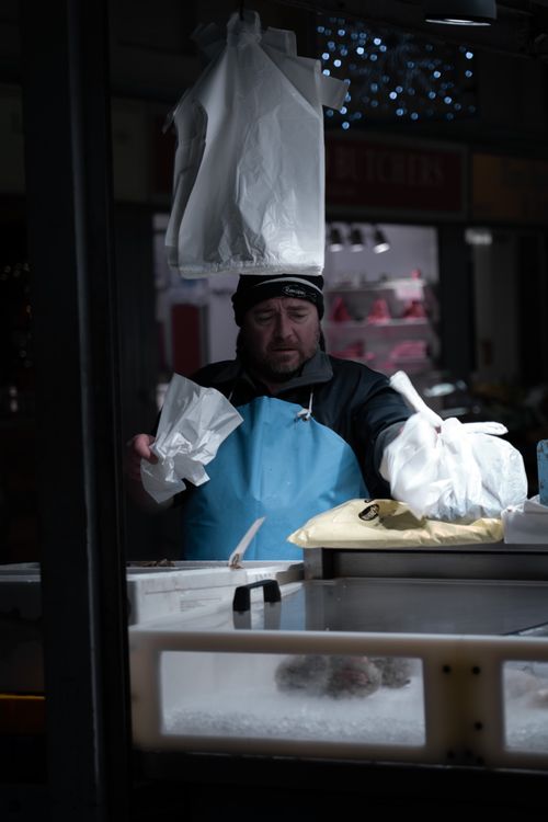 Free A vendor at a market preparing products in plastic bags under artificial light. Stock Photo
