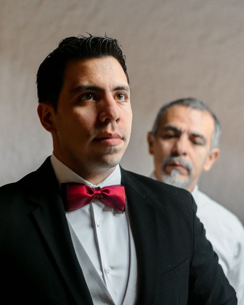 Free A groom in a suit with a red bow tie gets ready with assistance indoors. Stock Photo