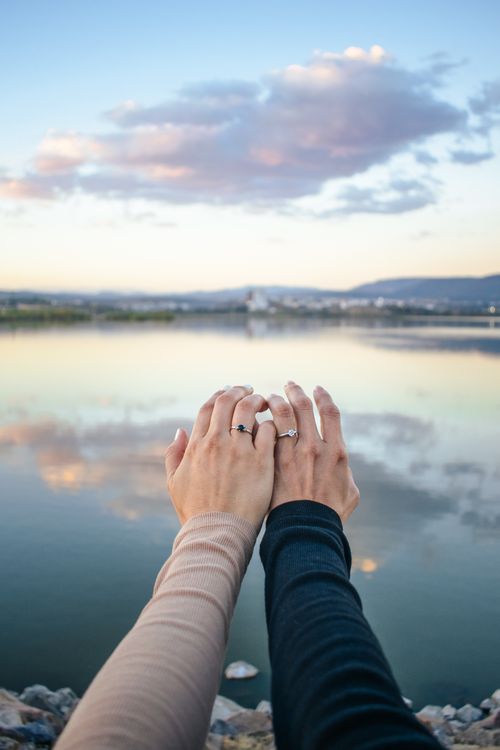 Free A romantic moment captured with a couple holding hands by a serene lake at sunset. Stock Photo
