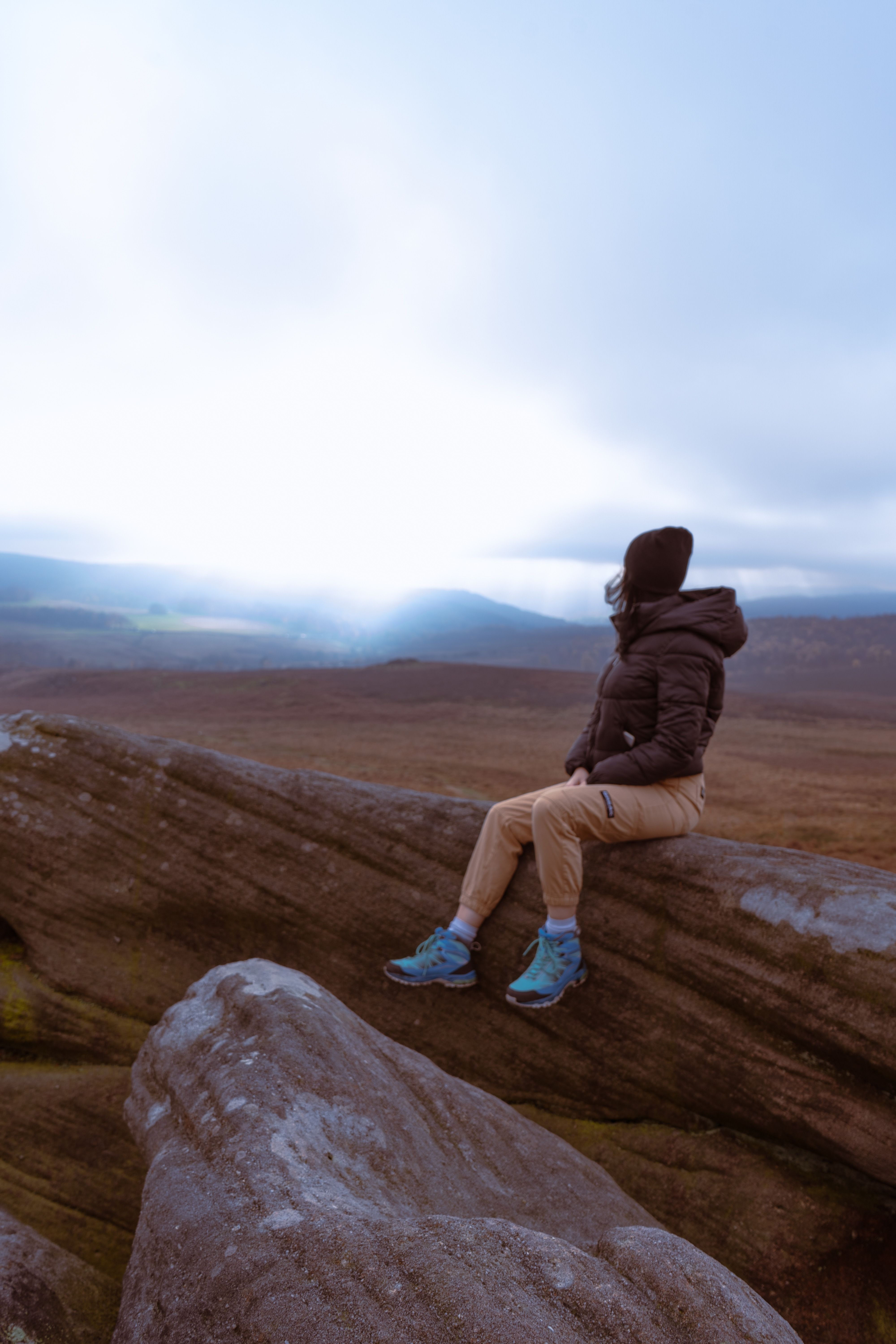 Person in Jacket Sitting on Rock with Plains behind · Free Stock Photo