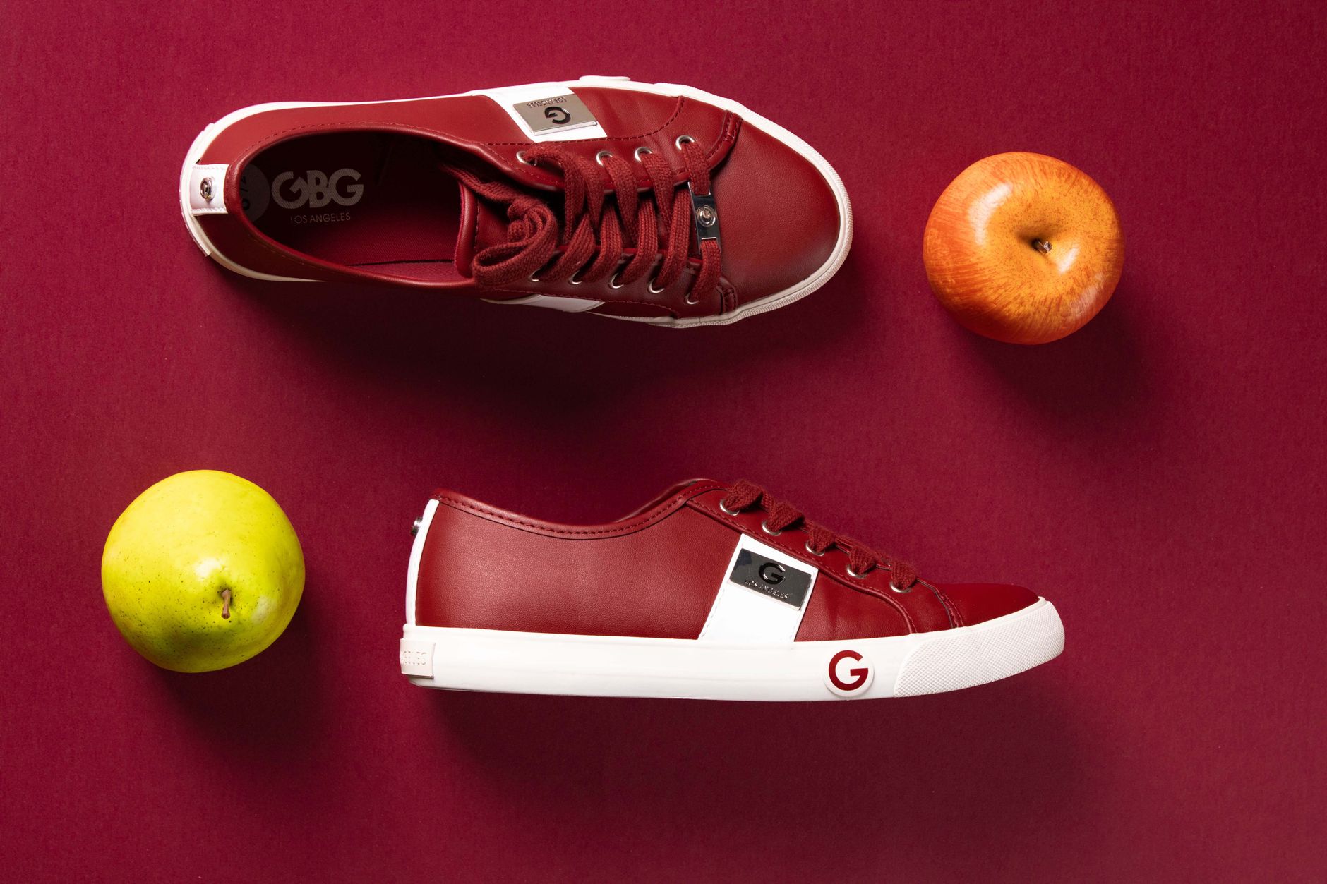 Stylish red sneakers paired with apples and pear on a vibrant red backdrop, highlighting modern fashion.