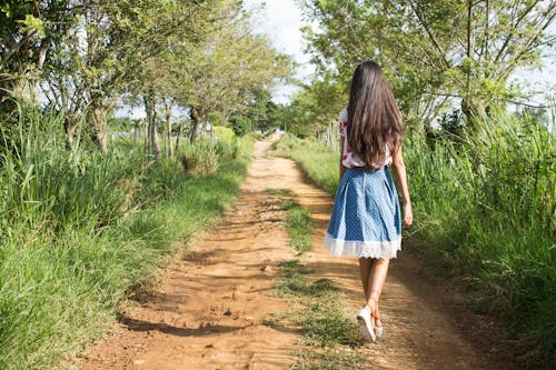 昼間に緑の草の近くを歩く青と白のスカートを着ている女性