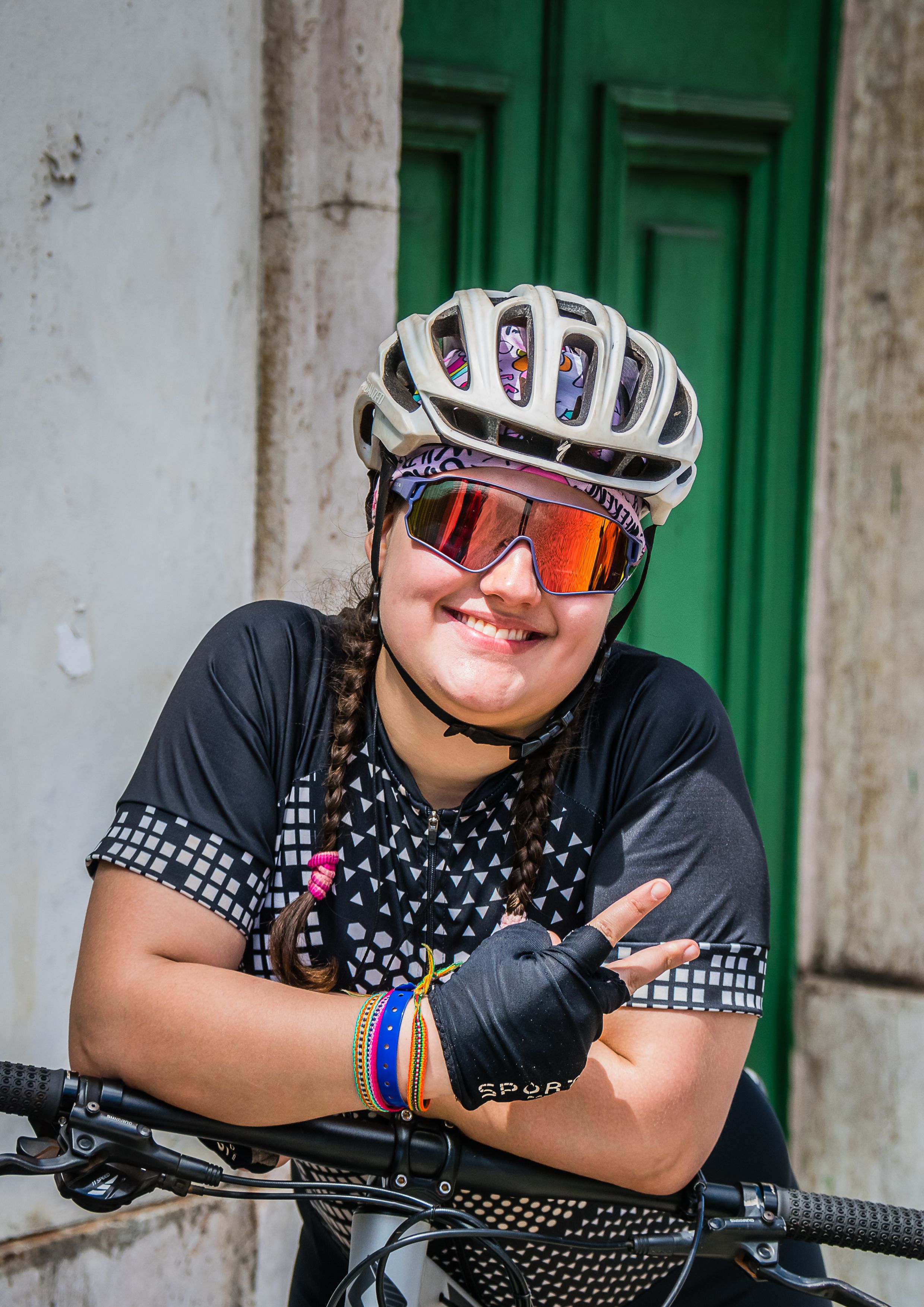 Smiling woman in cycling gear posing with peace sign and bright helmet.