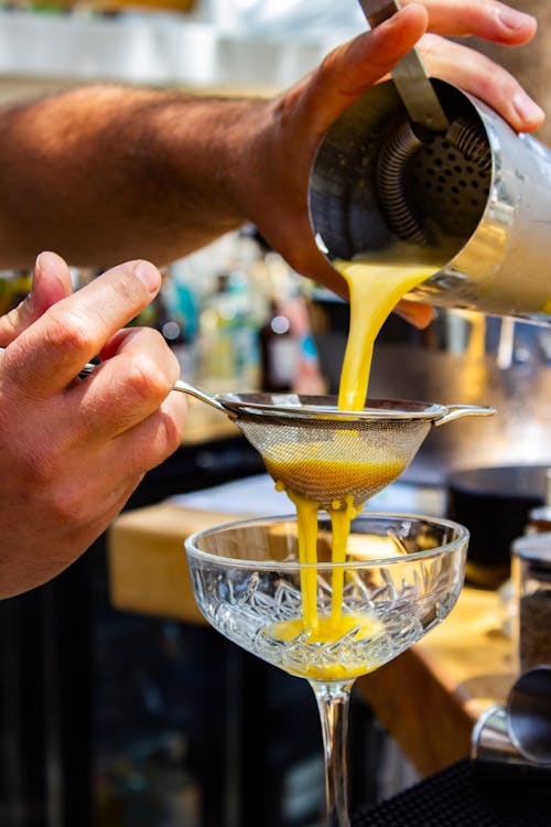 Hand Pouring a Drink through a Sieve