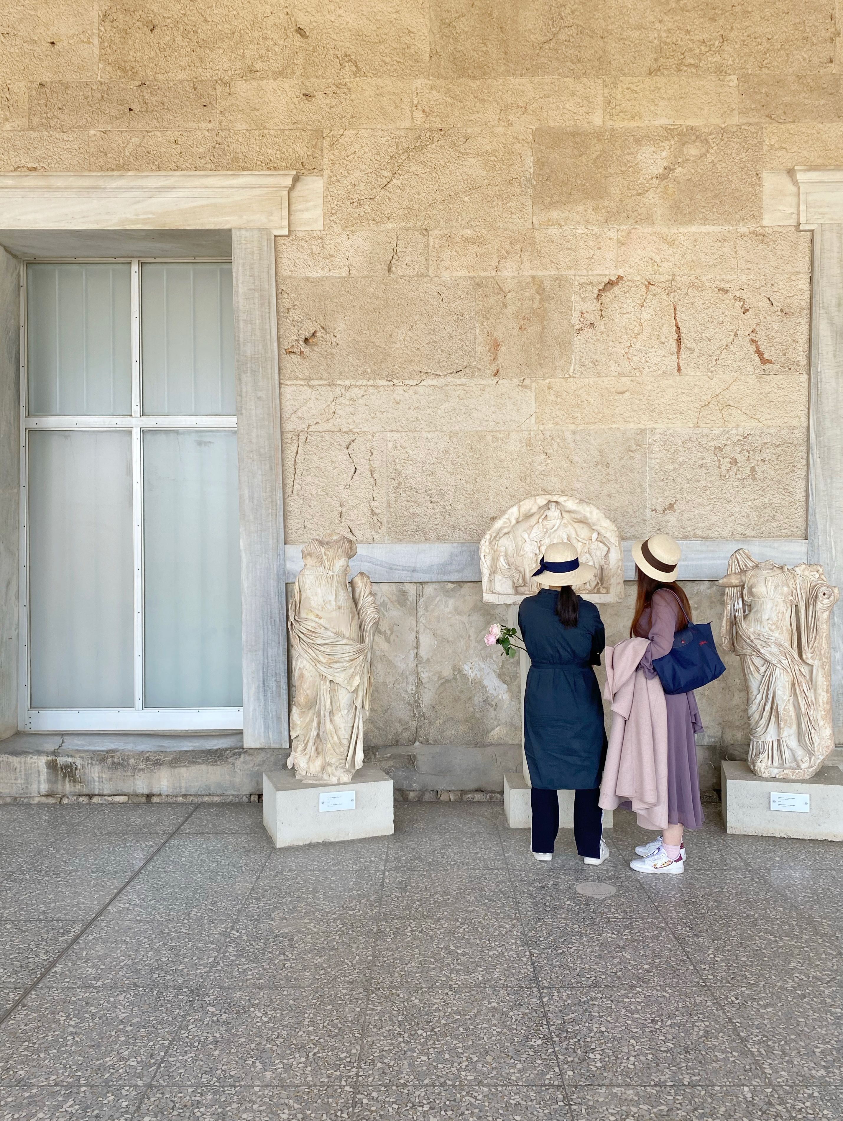 Two women admire ancient statues in a museum hallway, showcasing cultural appreciation.