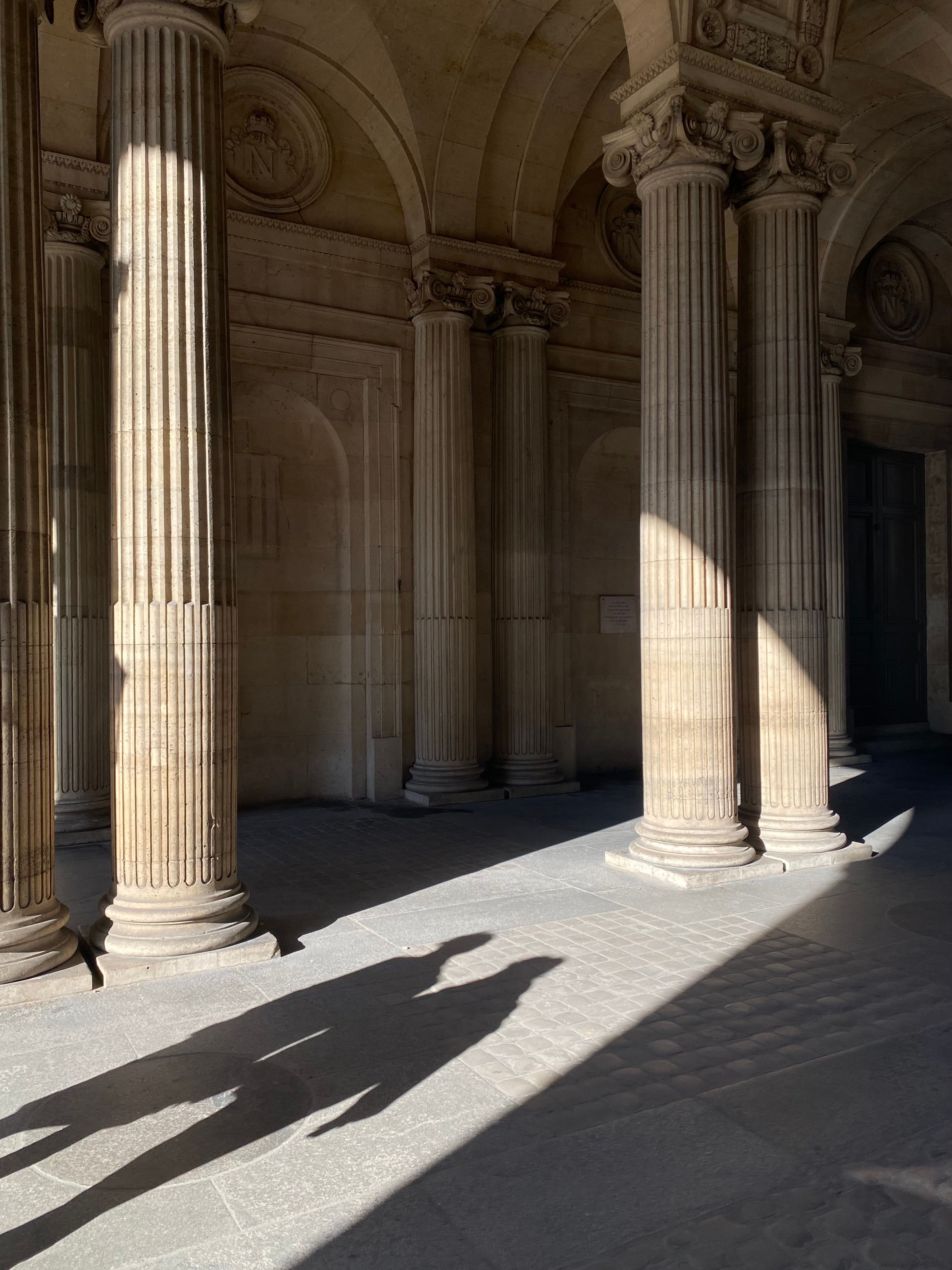 Dramatic sunlight casts shadows on classic columns in Paris, capturing an architectural marvel.