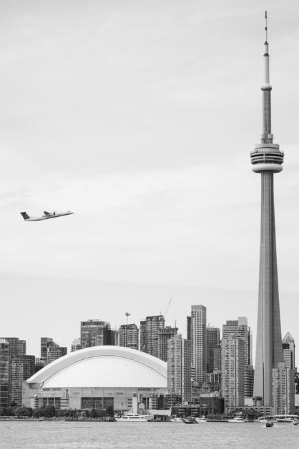 A stunning black and white view of Toronto's skyline featuring the CN Tower and Rogers Centre with an airplane overhead.