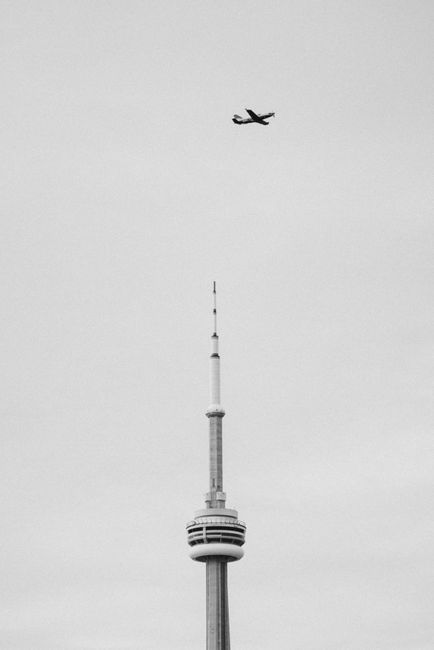A monochrome image of an airplane flying above the CN Tower in Toronto.