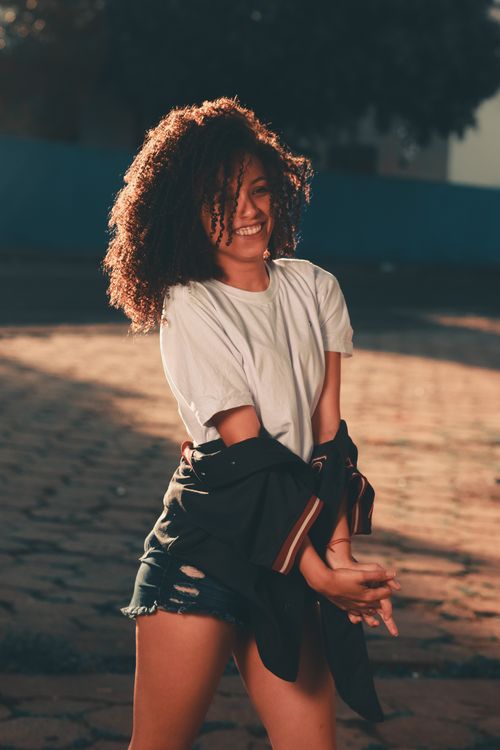 Free Smiling young woman with curly hair in casual summer attire, enjoying an urban outdoor setting. Stock Photo