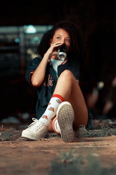 Young woman sitting outdoors, enjoying a drink with casual summer attire and sports socks.
